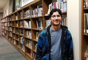 JHS student Afshan Chandani stands in front of library books.
