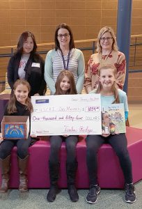 photo of three fifth grade girls presenting a check to an adult, along with their teacher and librarian