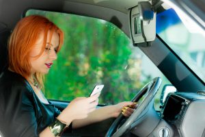 concept of danger driving. young woman driver red haired teenage girl texting on cell phone sending text reading message while driving the car.