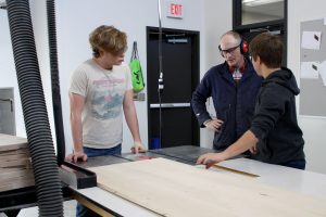 JHS Industrial Technology teacher Rhys South (center) consults with two students on the baseball locker project. 