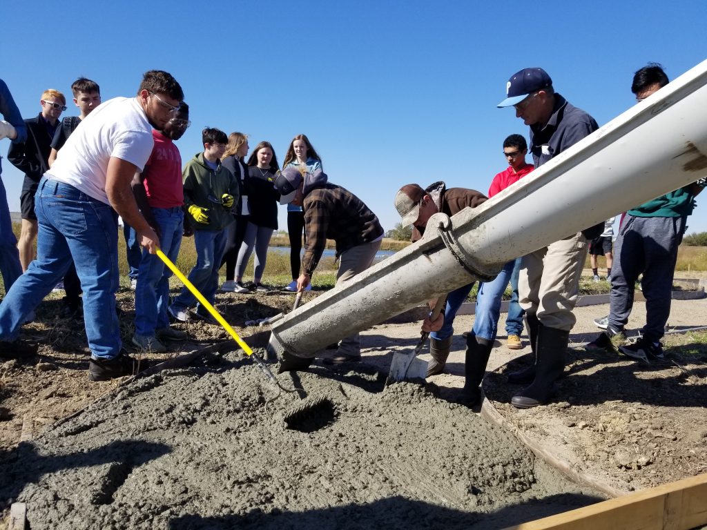 Students assist with a concrete pour. 