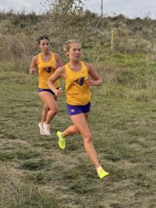 Two young women in yellow jerseys and purple shorts running in grassy field