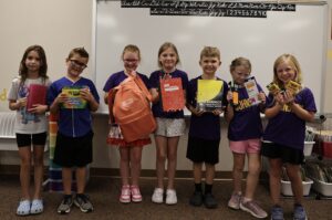 Group of seven elementary aged students holding school supplies
